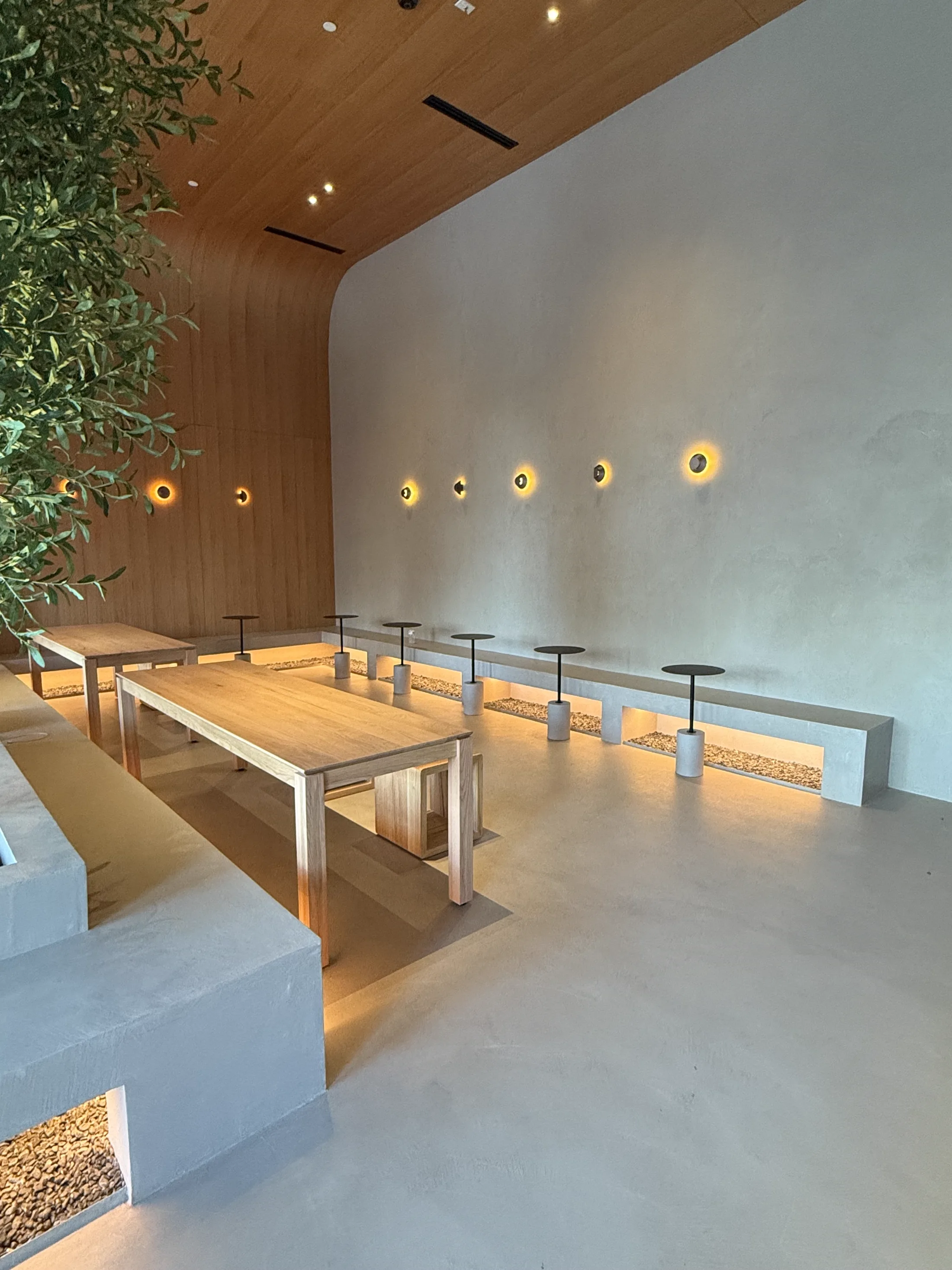 VOID interior, warm lights along a plaster wall above a long oak bench