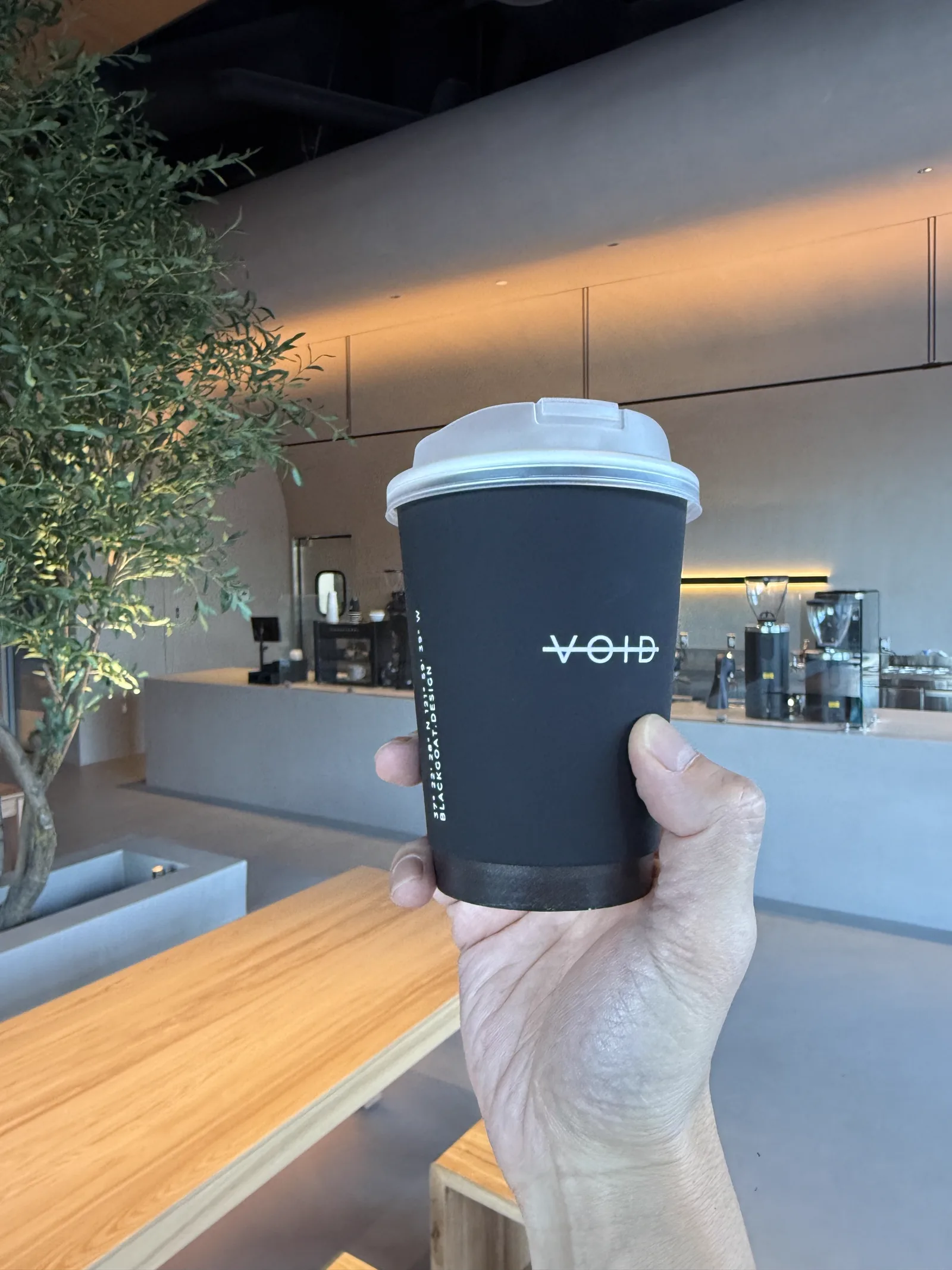 A matte black VOID cup held up against the warm interior